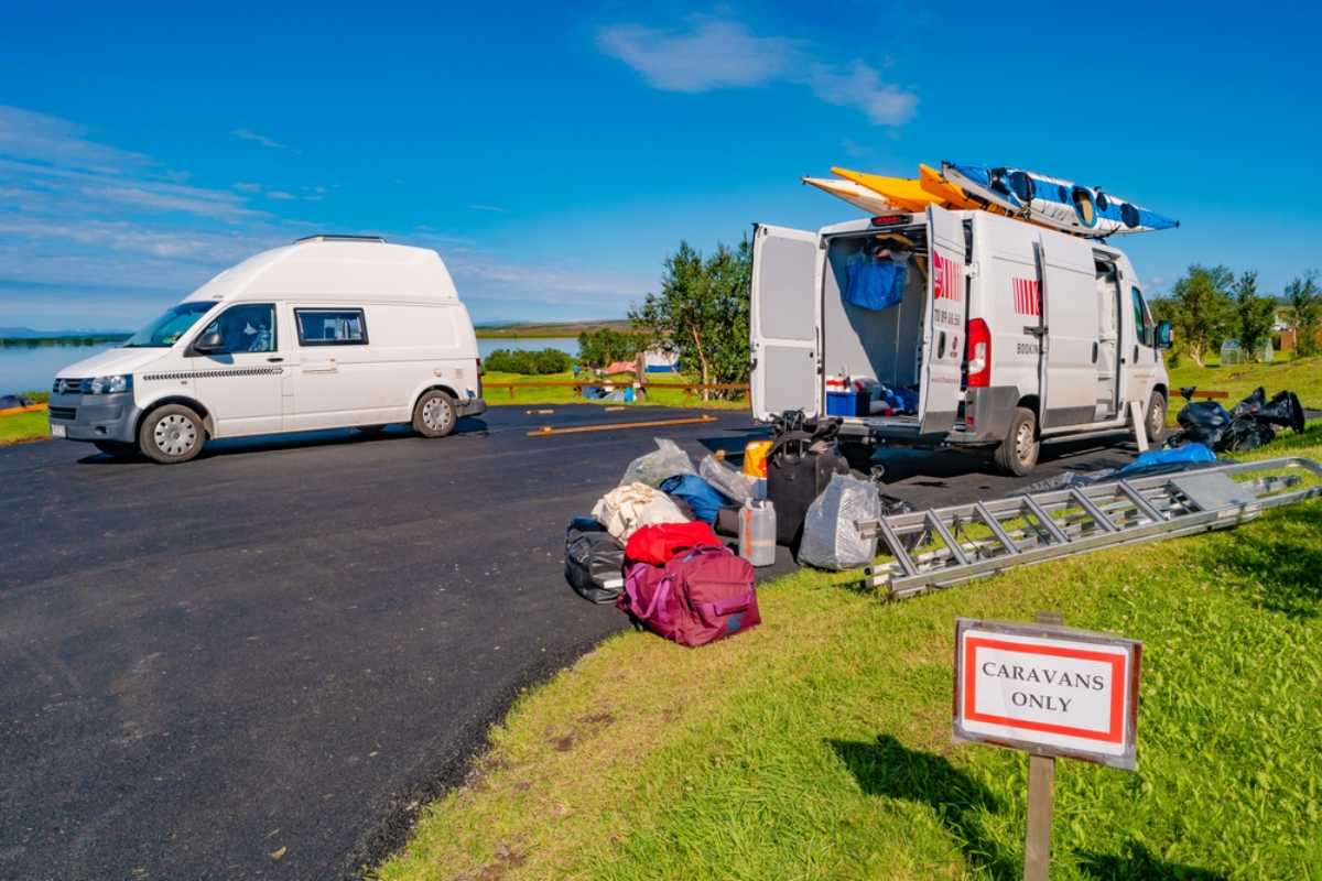 Two campervans parked at a campsite beside a sign that reads &ldquo;Caravans Only&rdquo;