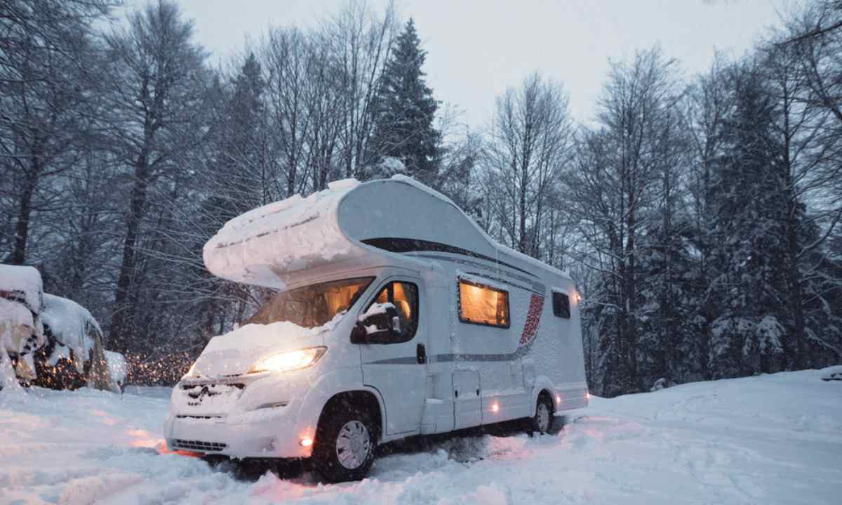 Winter camping in Iceland. Is it possible? Snow-covered motorhome parked in a forest clearing during heavy snowfall, warm interior lights glowing, typical winter camping in Iceland.