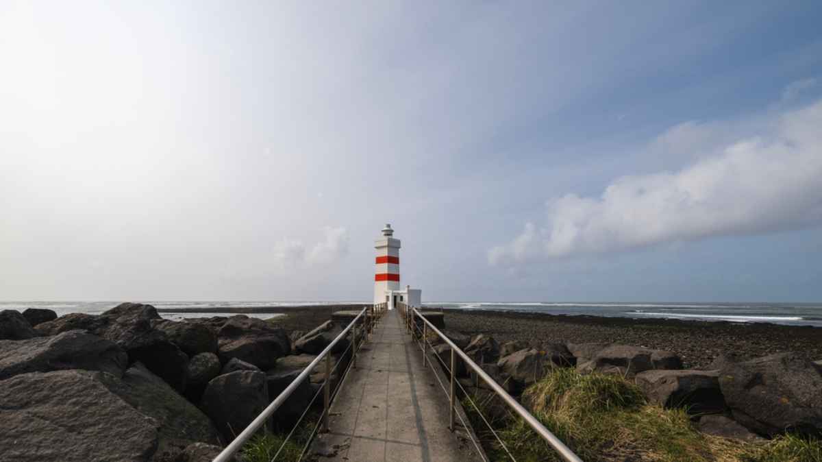 Red and white lighthouse on a rocky coastline in the Reykjanes Peninsula.