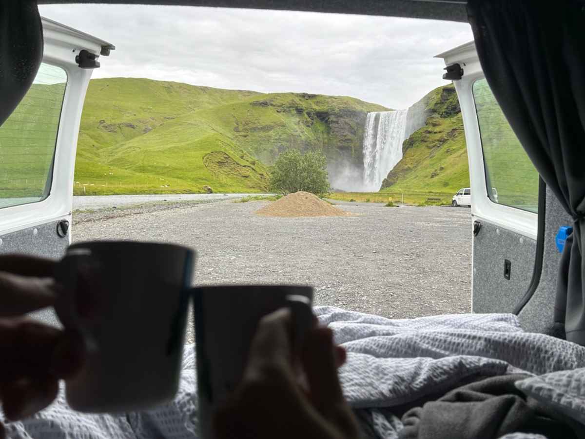 View of Sk&oacute;gafoss waterfall from the back of a campervan with coffee mugs in the foreground.