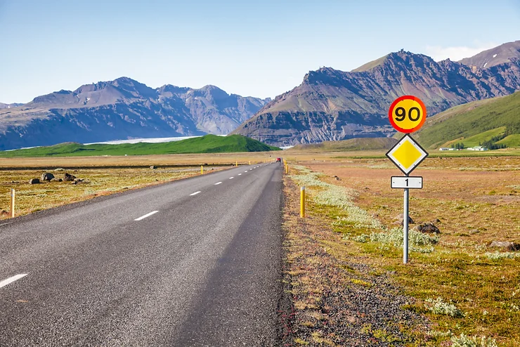 Un panneau de limitation de vitesse de 90 en Islande sur le bord d'une route rurale déserte avec des montagnes au loin.