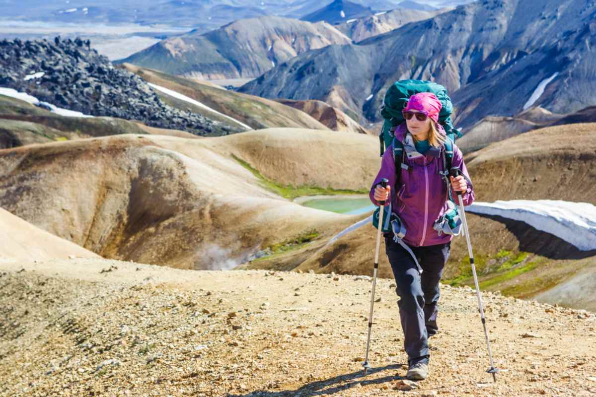 A mountaineer in hiking clothes and gear walks straight ahead in an imposing Icelandic rugged landscape.
