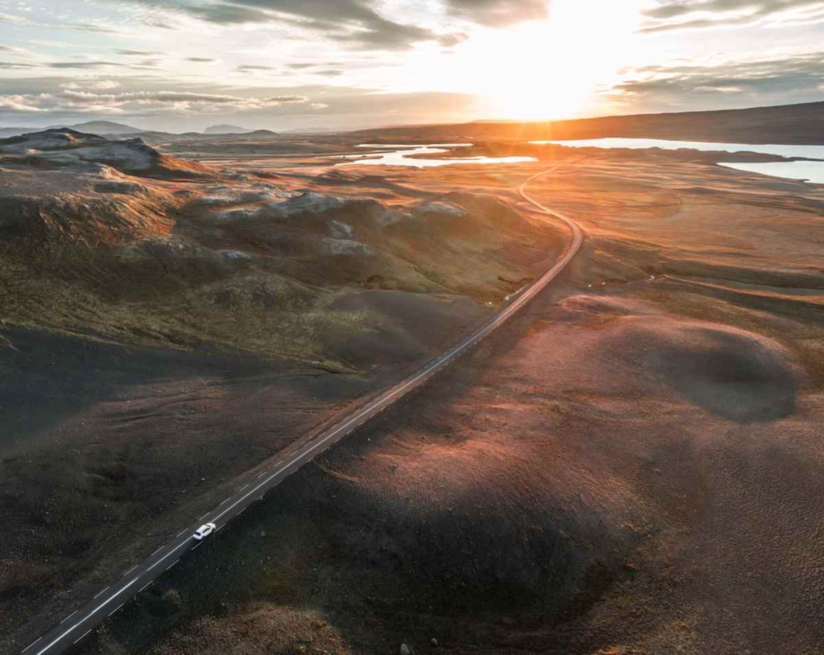Aerial view of a vehicle driving on a deserted Icelandic road at sunset. 