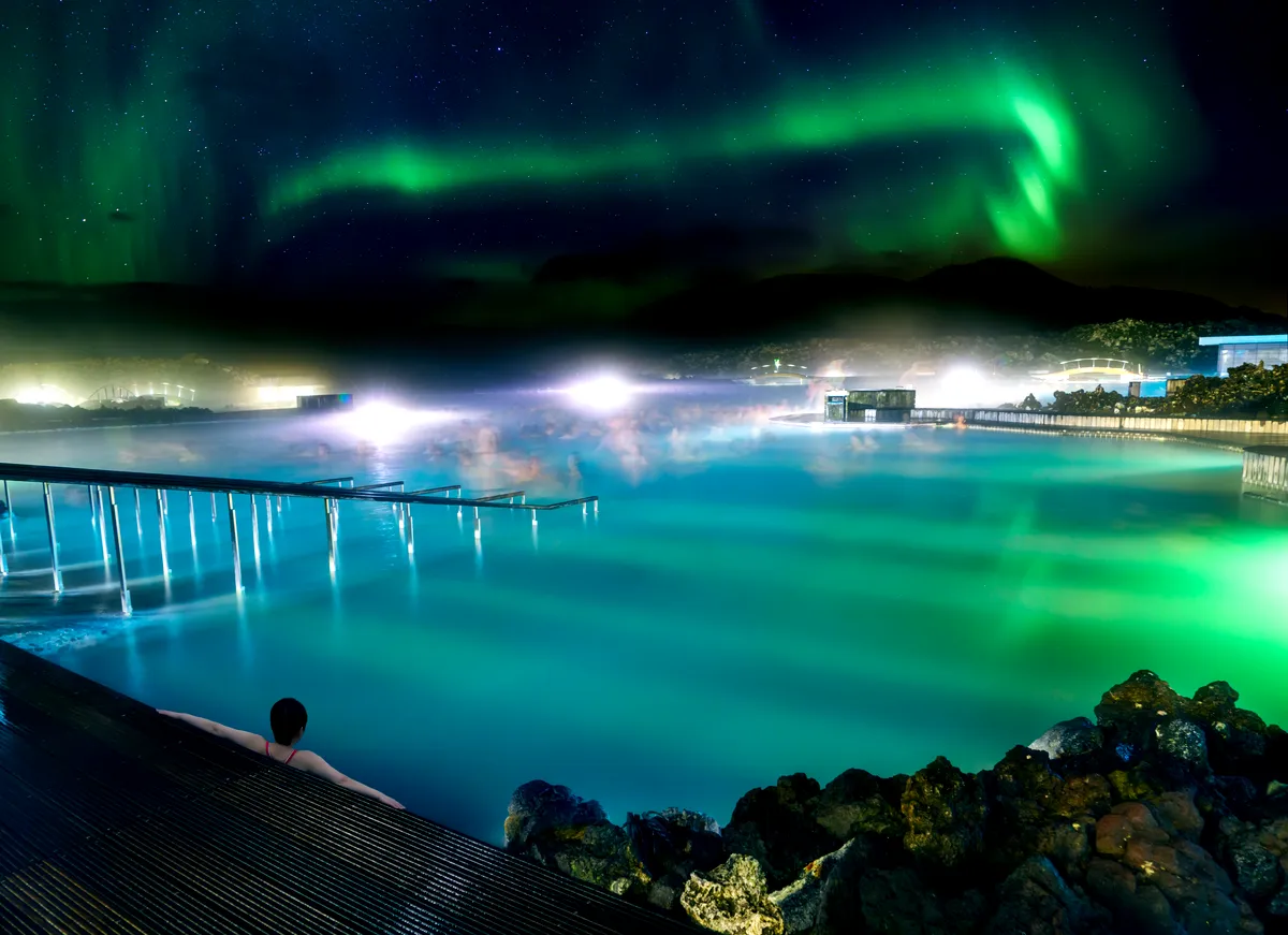 The Blue Lagoon under a sky illuminated by the Northern Lights, with steam rising from the geothermal waters.