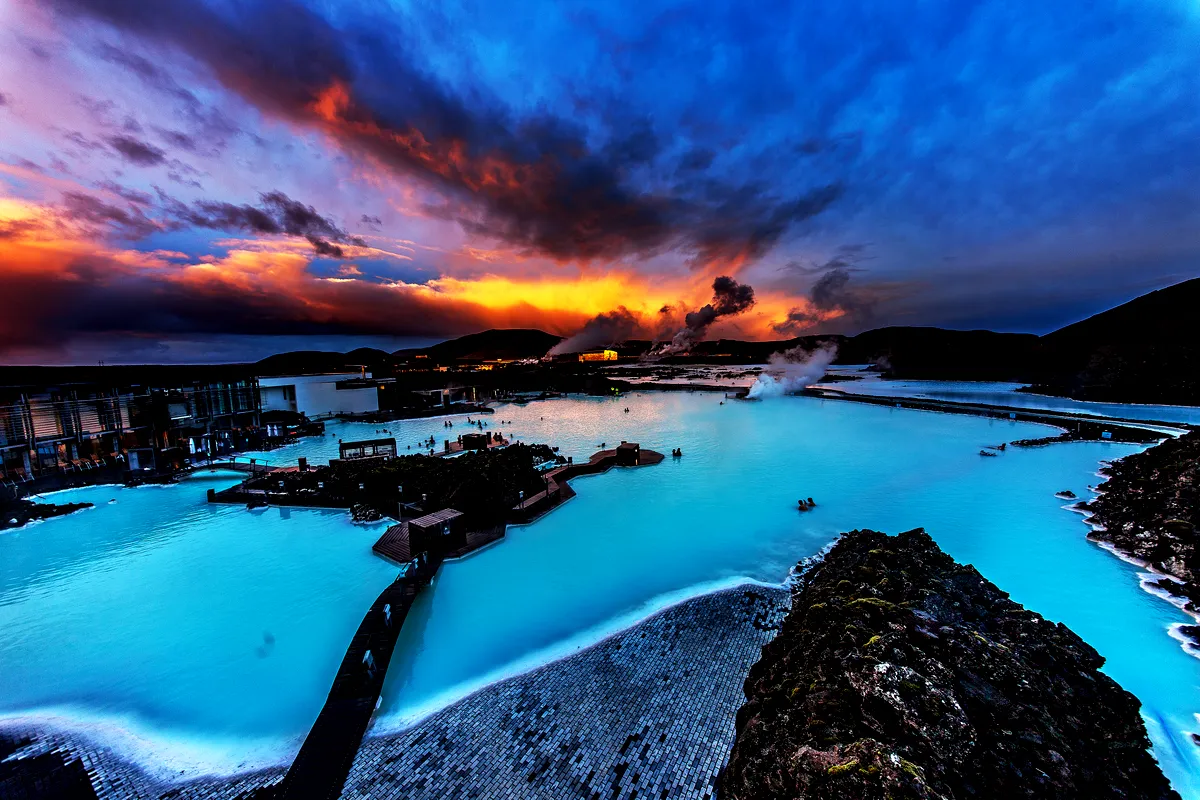 A beautiful sunset casts vibrant colors over the Blue Lagoon, with steam rising from the thermal waters.