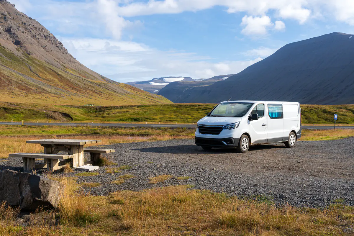 A white campervan parked at a designated rest area in Iceland, with mountains and a glacier in the background. Following Iceland’s camping laws, the vehicle is parked in an authorized spot to avoid fines and environmental damage.
