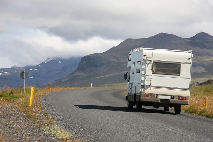 A campervan driving along a scenic road in Iceland, surrounded by mountains and dramatic landscapes—highlighting the freedom and adventure of campervan travel on the island.