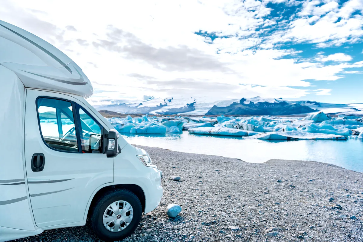 An RV parked beside the serene Glacier Lagoon in Iceland with icebergs floating in the background.