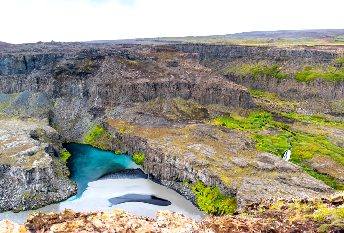 Hikers standing at the edge of J&ouml;kuls&aacute;rglj&uacute;fur Canyon, overlooking the vibrant blue waters and dramatic cliffs