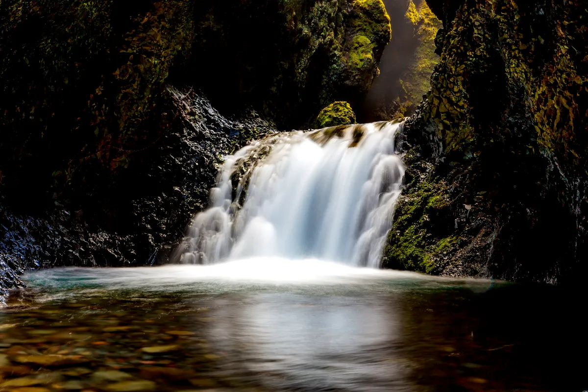 A hidden waterfall flows between rugged rocks in Nauthúsagil, Iceland