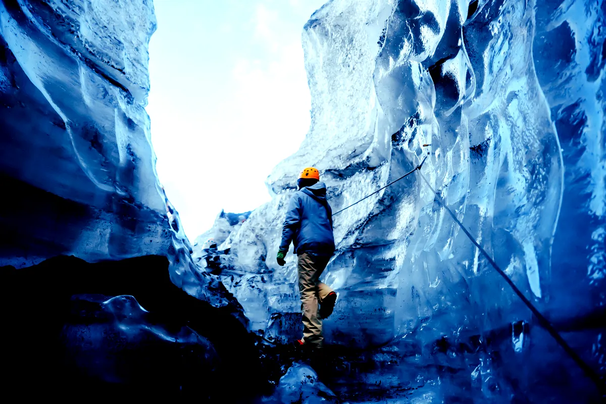 A hiker walking through the narrow icy passages of Katla Ice Cave, Iceland, surrounded by vibrant blue ice walls.