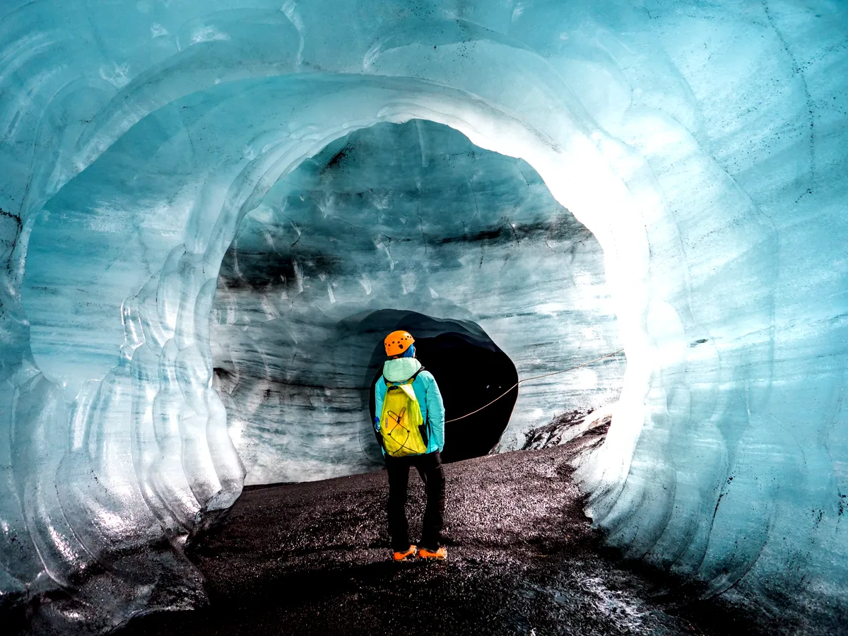 Person in a yellow backpack exploring the heart of Katla Ice Cave, Iceland, illuminated by sunlight filtering through the icy archway.