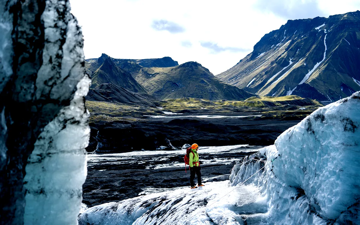Hiker standing on a glacier near Katla Ice Cave, Iceland, with a backdrop of rugged mountains and icy terrain.