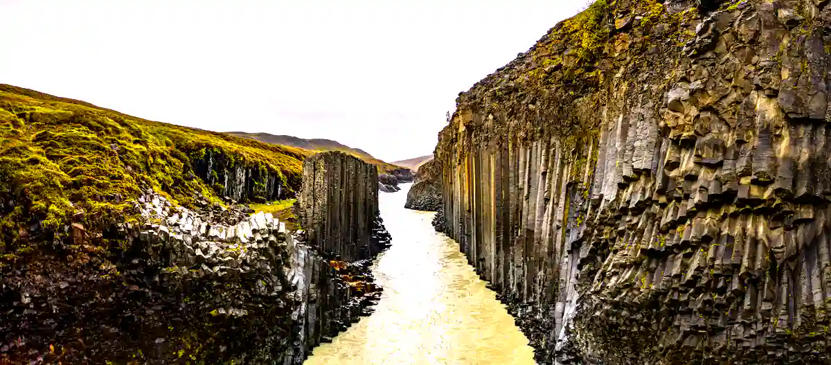 A stunning landscape view of Studlagil Canyon with its basalt cliffs and vibrant green moss.