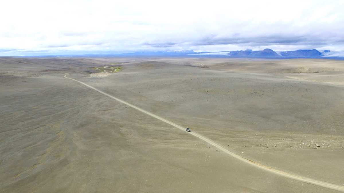 A vehicle is seen from afar in what looks like a dry desert landscape on the island of Iceland.