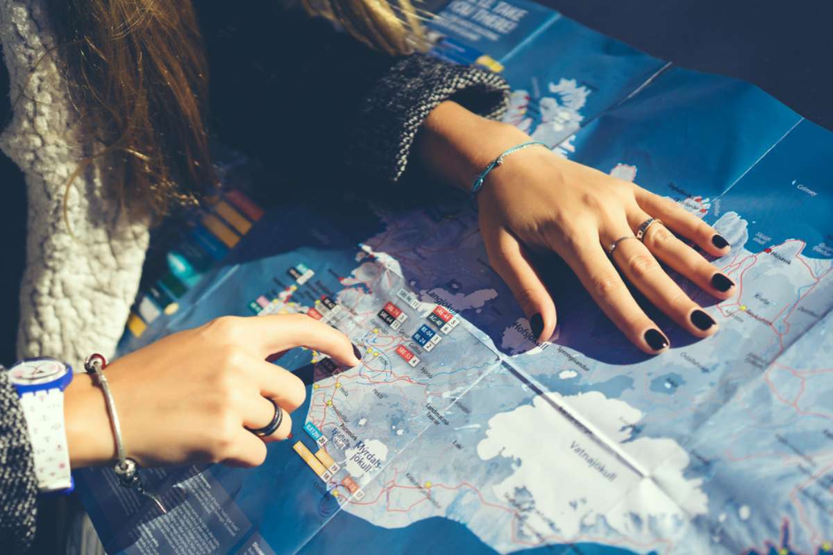 Close-up of hands planning an Iceland road trip route on a paper map, pointing at destinations and roads.