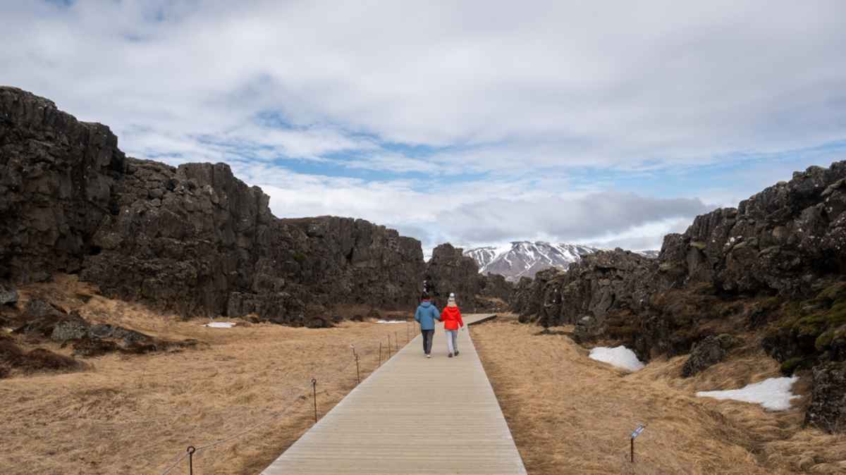 A hiking couple walks through Thingvellir National Park in Iceland, known because two tectonic plates merge beneath it.