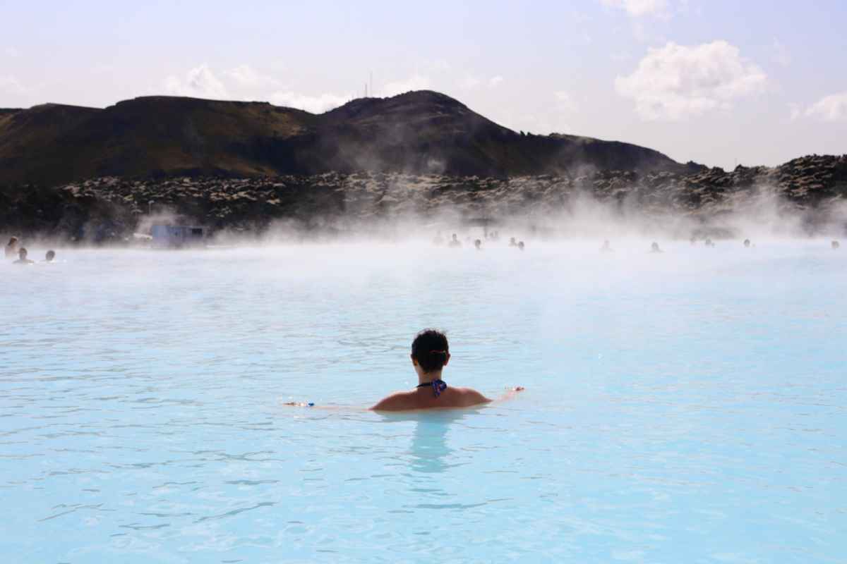 A woman with her hair up takes a relaxing swim in Iceland's Blue Lagoon on a sunny day.