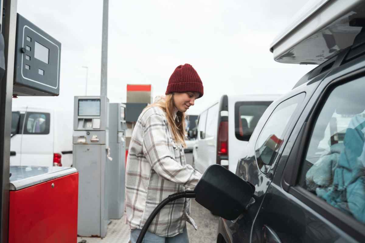 A woman in a plaid shirt and cap refuels at a gas station in Iceland.