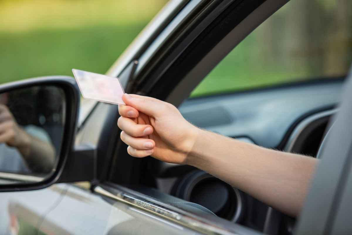 Une personne passe son bras par la fenêtre baissée d’une voiture en tenant ce qui semble être son permis de conduire.