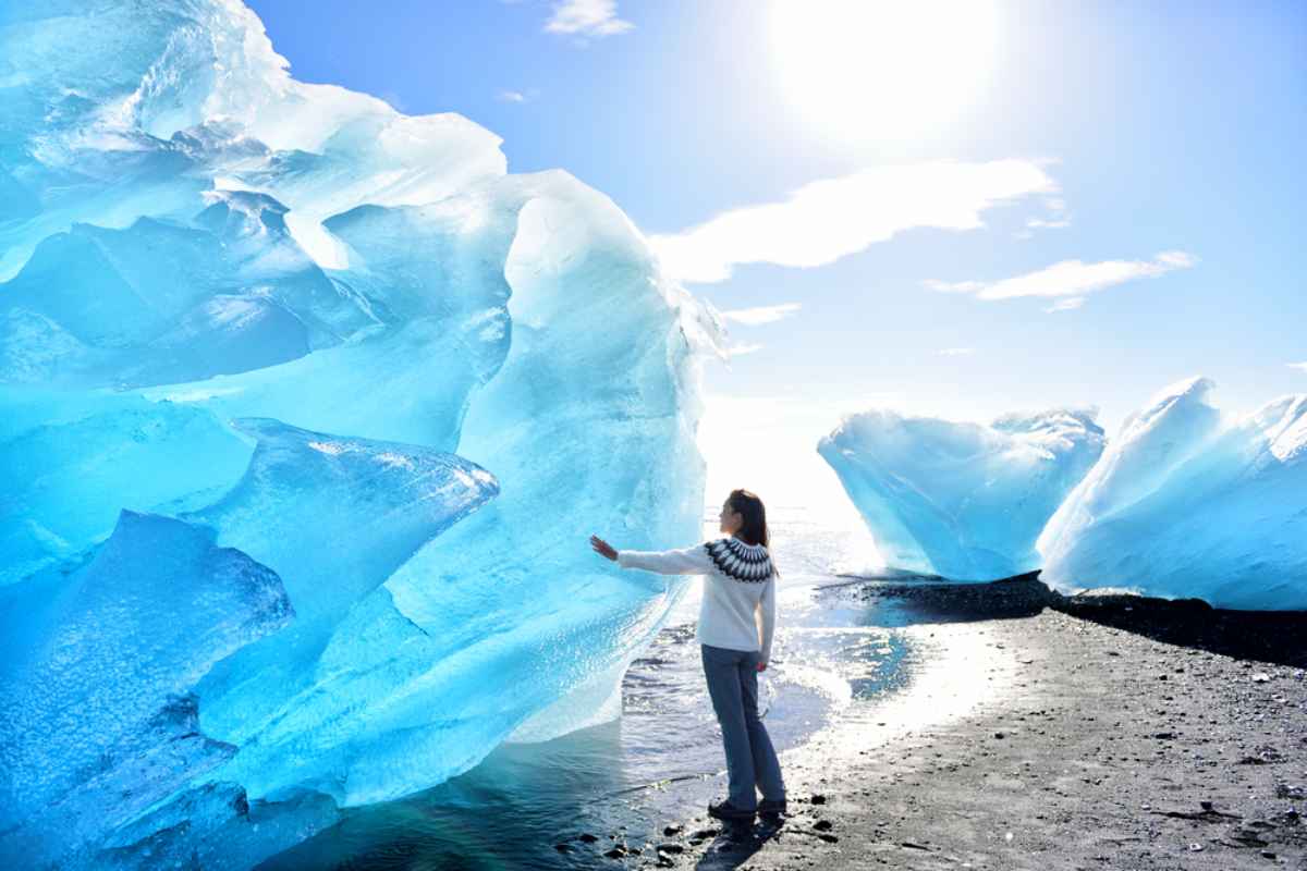 Une femme minuscule touche du bout des doigts l’un des magnifiques et imposants blocs de glace sur Diamond Beach en Islande.