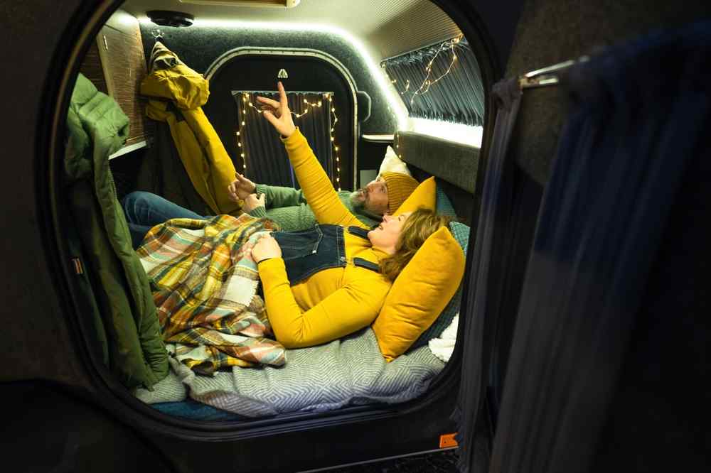 Mini camper at night in Iceland Couple relaxing inside a cozy mini camper with blankets and string lights.