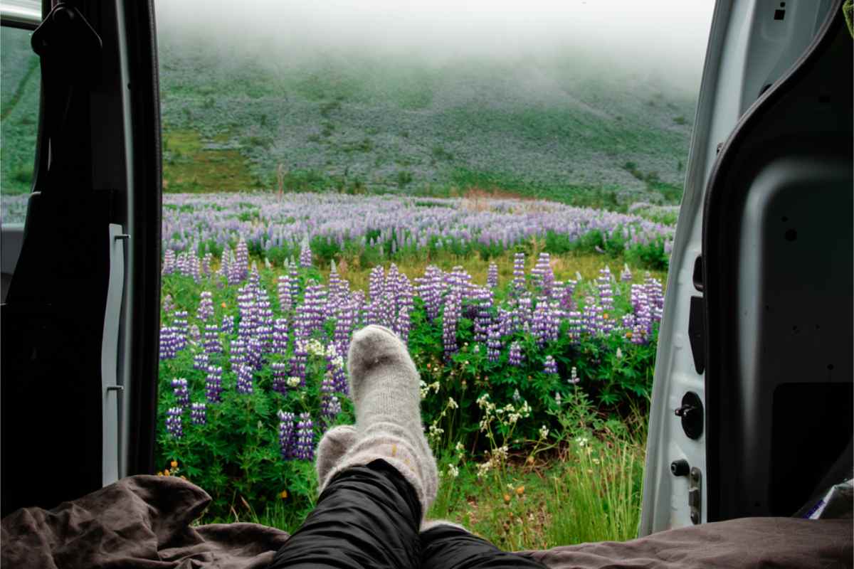 Tourist with her feet up in her campervan, doors wide open, with a beautiful spring landscape