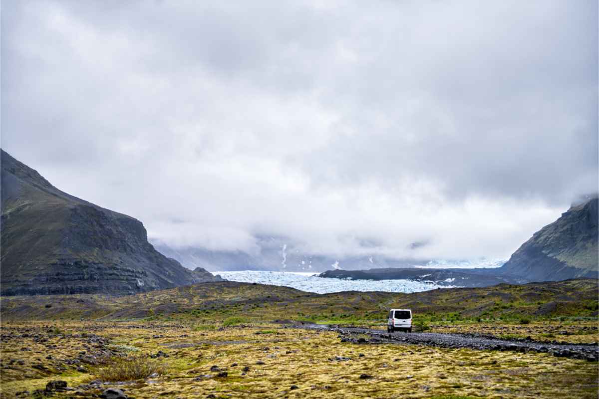 White campervan driving off in Iceland's impressive landscape with a glacier on the background