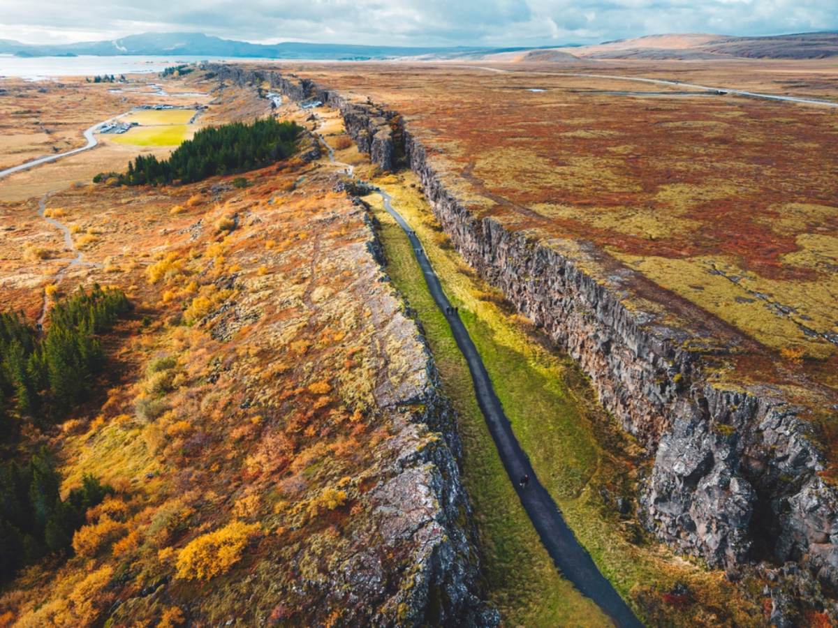 Rift valley path in Þingvellir National Park Aerial view of a footpath running between tall basalt walls through autumn-coloured moorland, with a lake in the distance