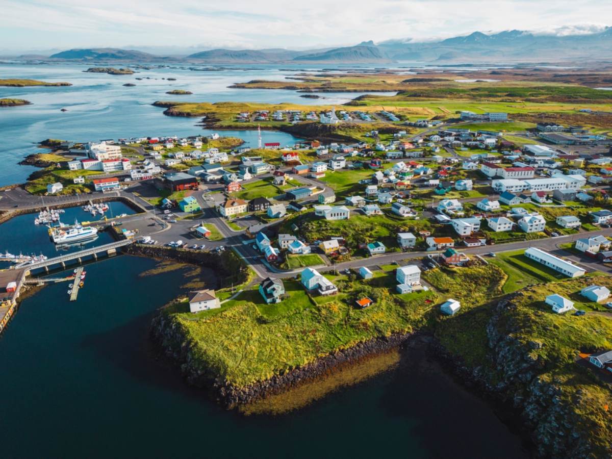 Fishing town on the Snæfellsnes peninsula Aerial view of a colourful coastal town with a harbour and fishing boats, surrounded by islands and distant mountains