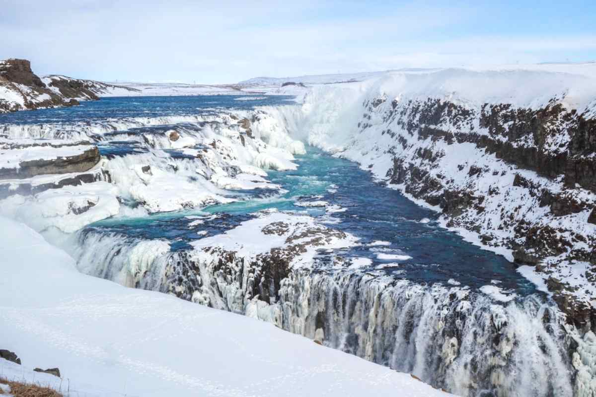 Gullfoss waterfall partially frozen, turquoise water rushing through a snowy canyon.