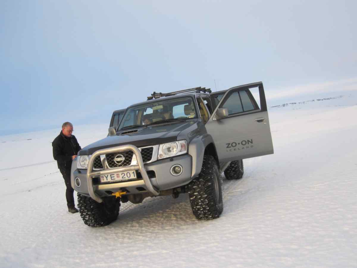 Man standing beside a lifted Nissan 4x4 with oversized snow tires on an Icelandic snowfield during a Super Jeep tour.