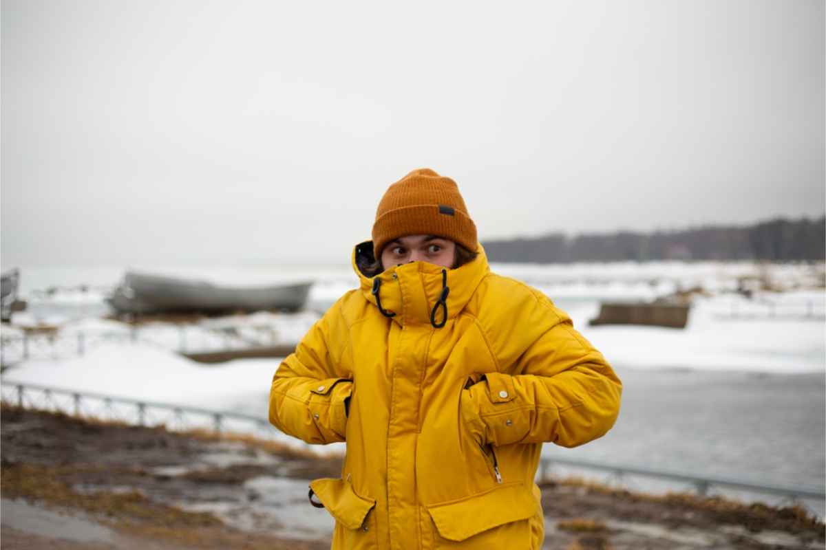 young man feeling cold and covering himself with a thick yellow jacket