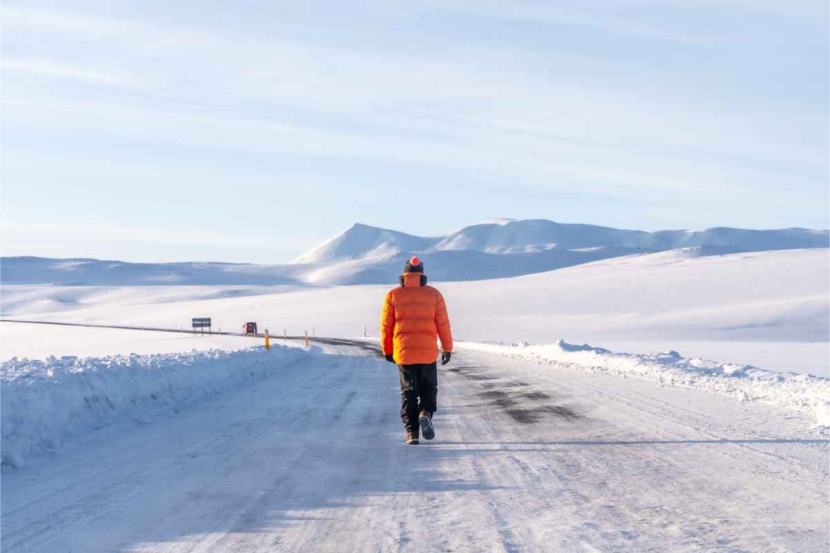 Winter landscape in Iceland with a man in orange jacket walking on a road covered in snow
