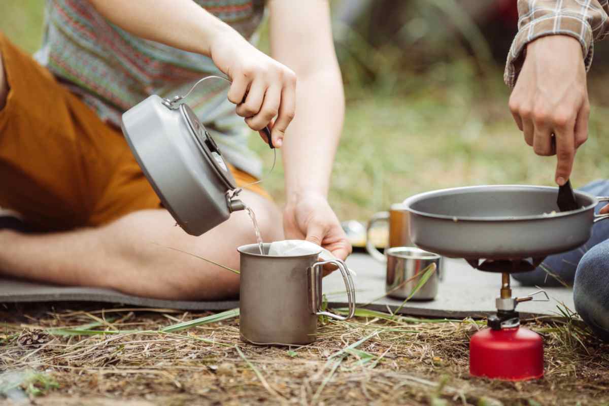 Pouring hot water into a mug beside a backpacking stove while camping.