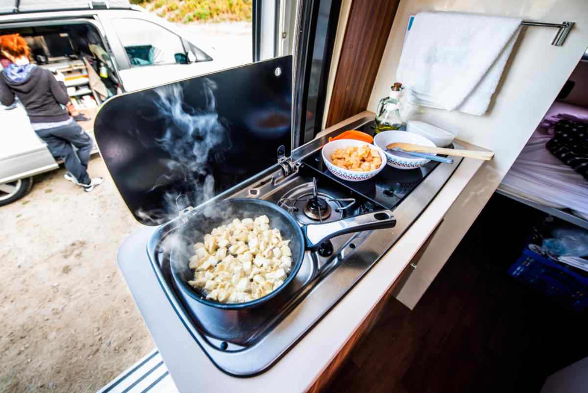 Compact campervan kitchen with a gas stove and steaming skillet while parked.
