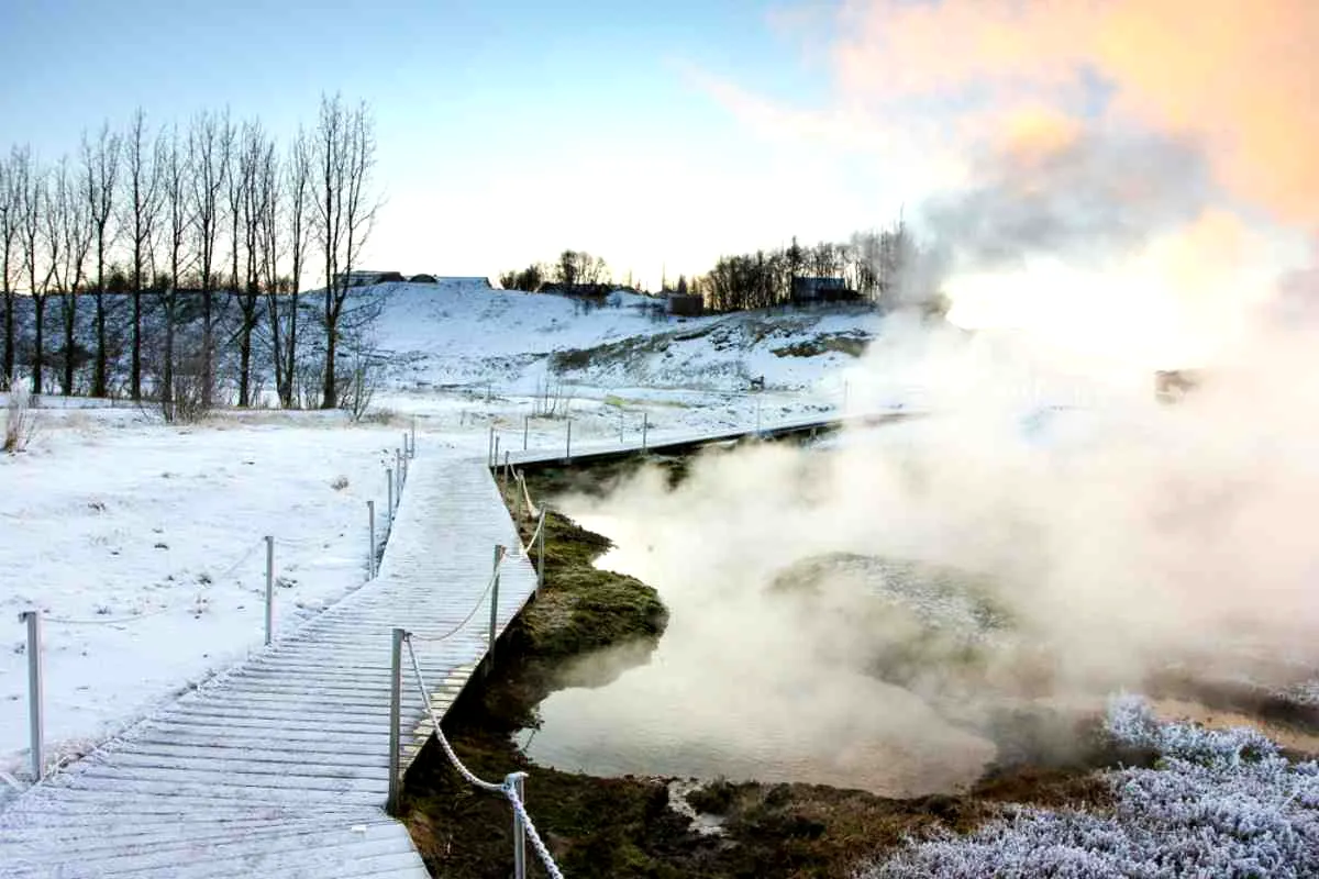 Pasarela nevada junto a aguas humeantes de la Secret Lagoon en pleno invierno.