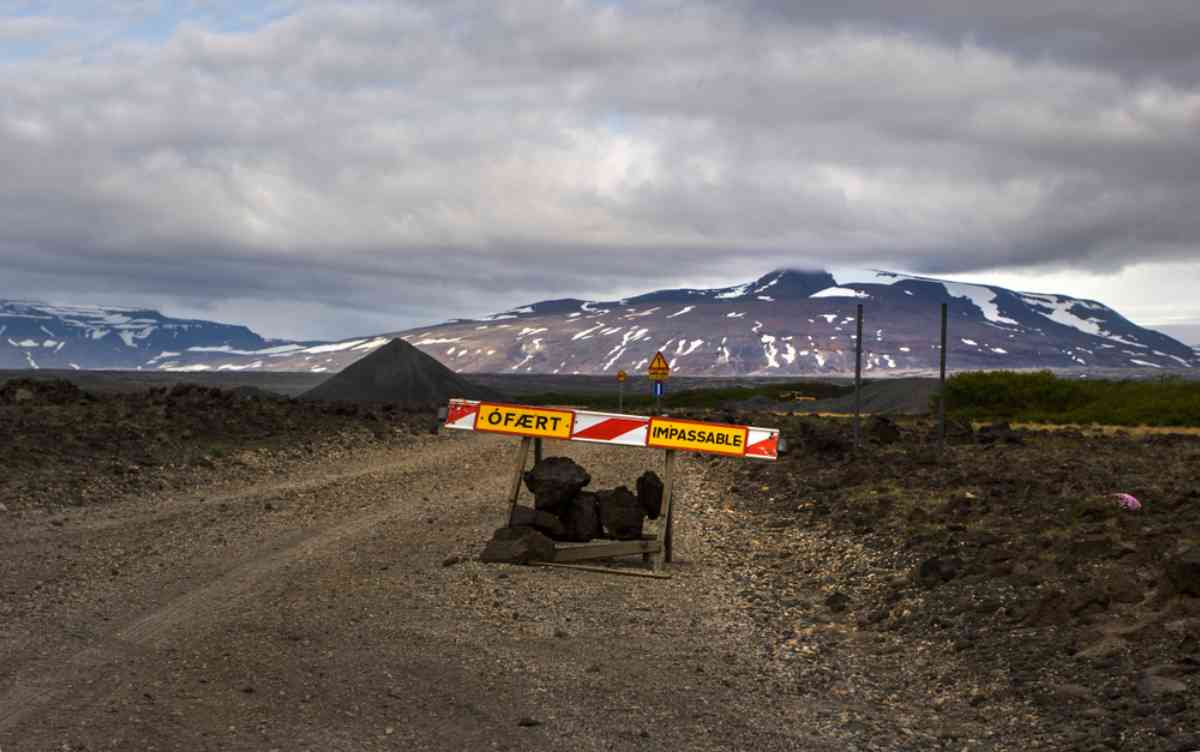 Road closures in Iceland Road-closure barrier reading “Ófært / Impassable” on a gravel highland track with snowy mountains in the background.