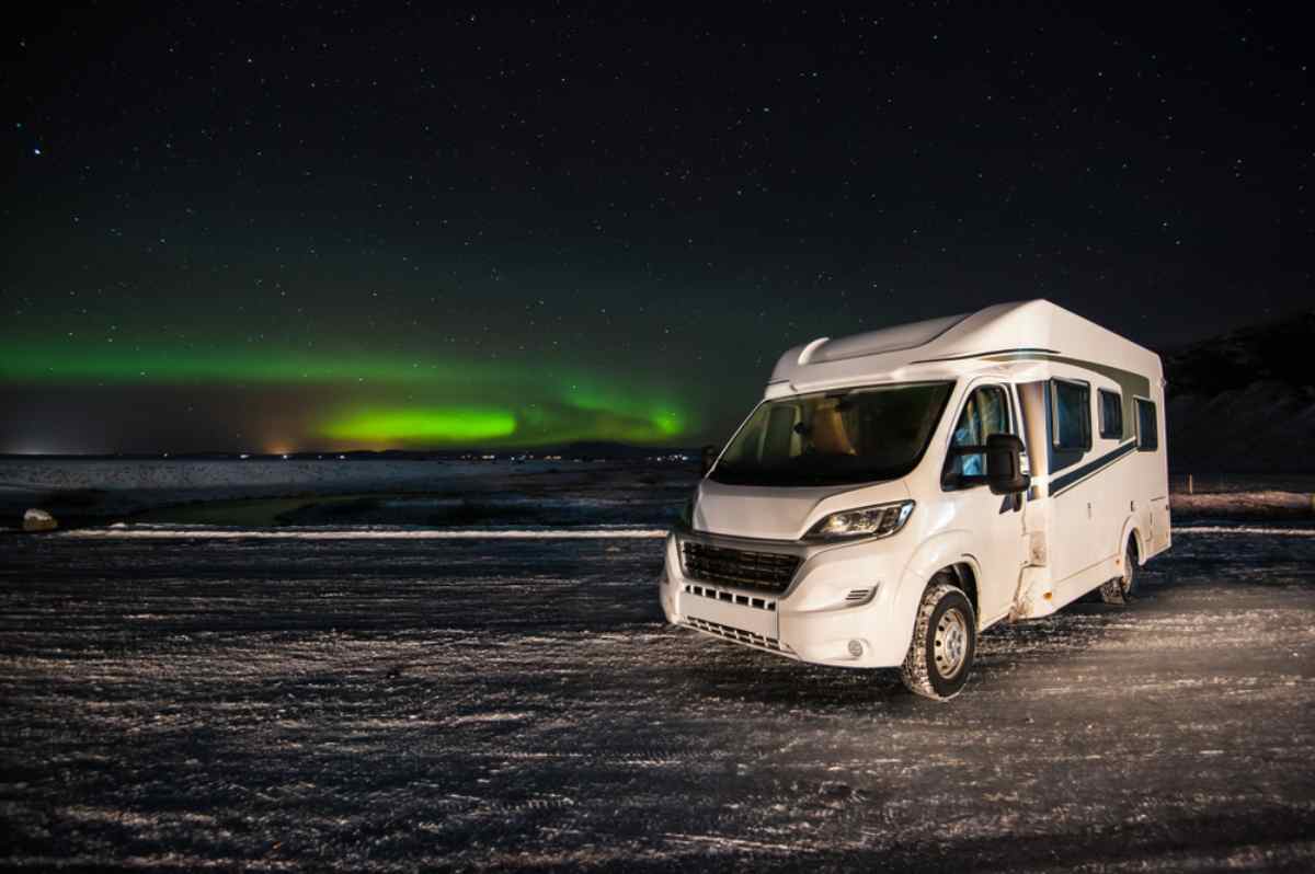 Auroras boreales en Islandia Autocaravana estacionada sobre nieve bajo auroras boreales en Islandia; cielo estrellado y resplandor verde, escena invernal perfecta para viajar por libre.