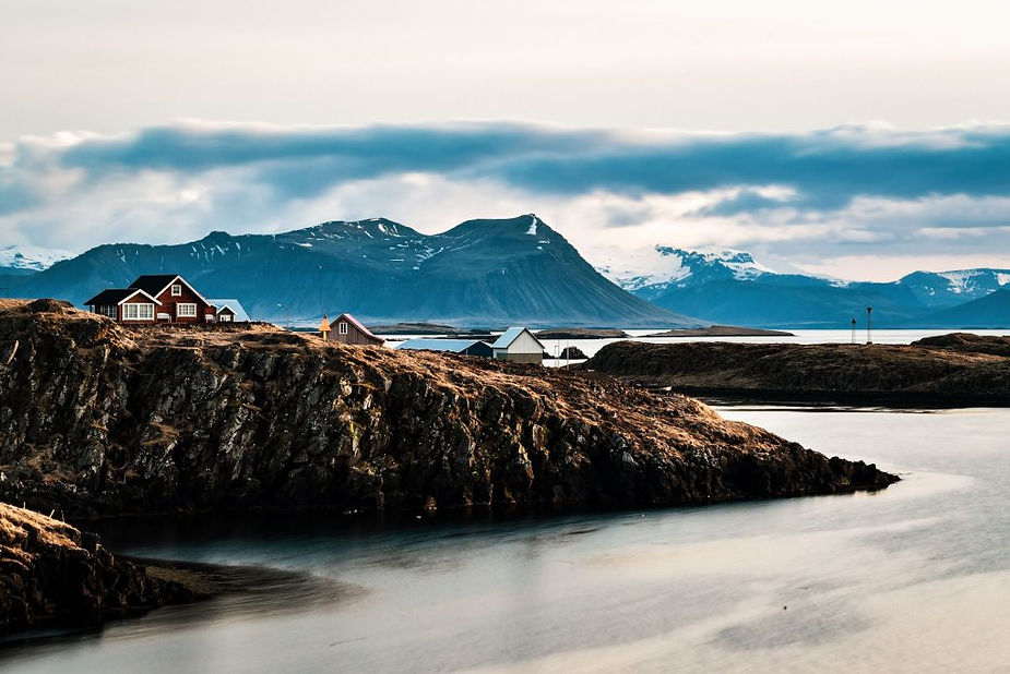 Case sulla costa di Stykkishólmur affacciate su isole rocciose e fiordo calmo, montagne innevate all’orizzonte.