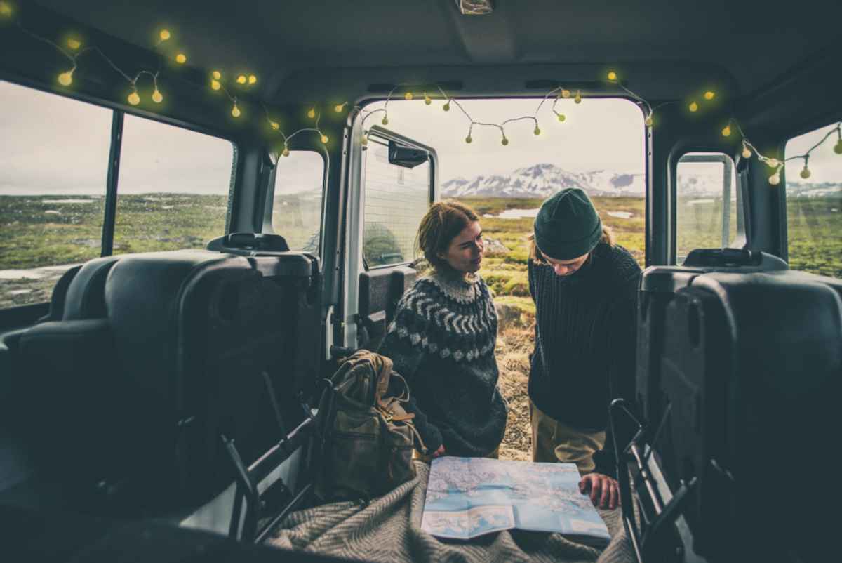 Van e mappa Coppia dentro un van con lucine, maglioni islandesi e mappa aperta; pianificazione dell’itinerario invernale tra valli e cime innevate.