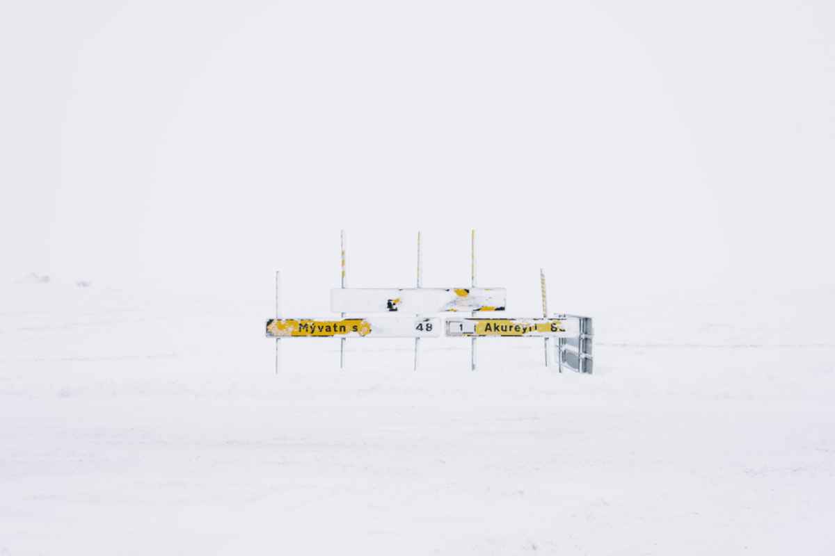 Segnaletica innevata Cartelli stradali verso Mývatn e Akureyri quasi sommersi dalla bufera; visibilità minima e paesaggio completamente bianco nel nord dell’Islanda.