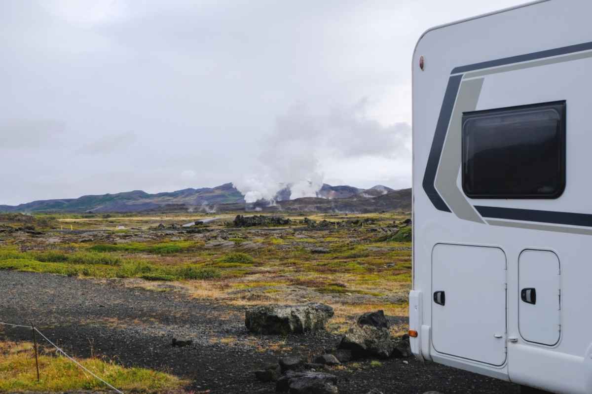 Lato di un camper con vista su campo geotermico islandese e colonne di vapore sullo sfondo.