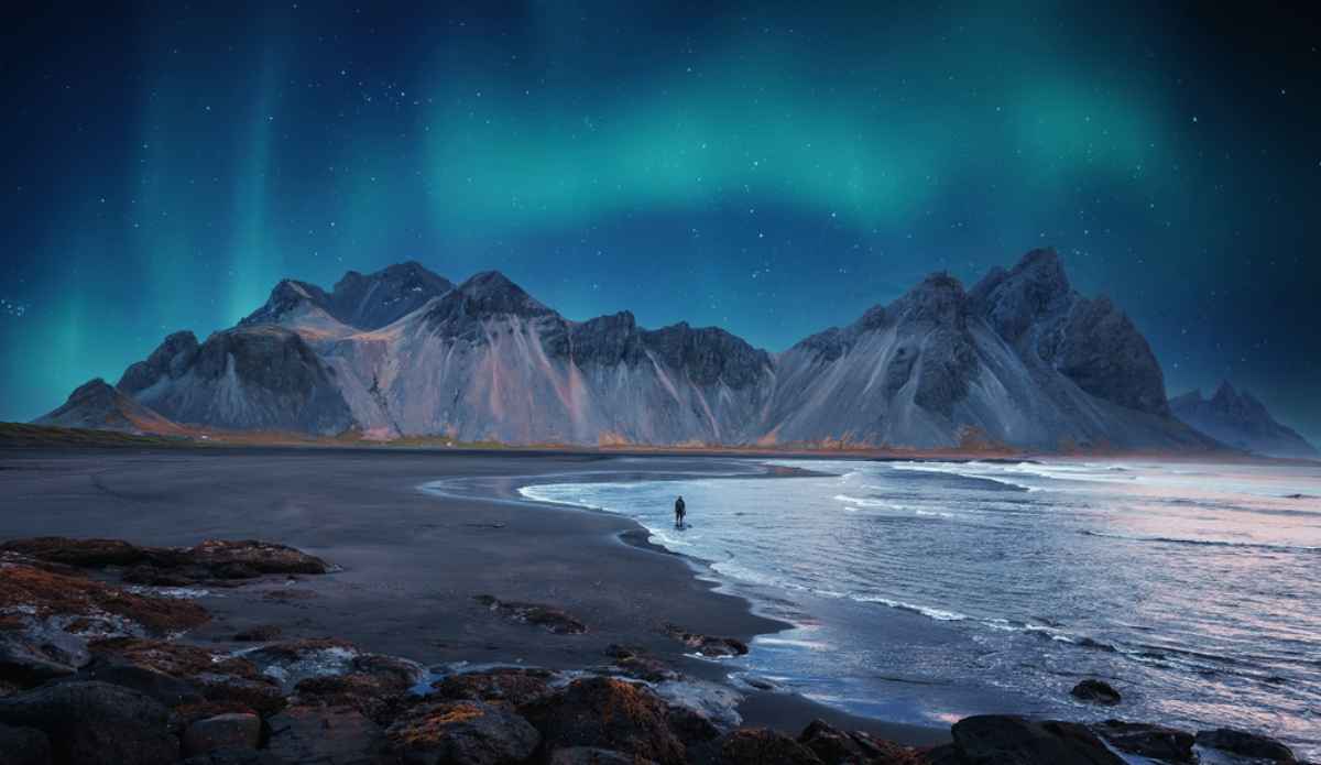 Spiaggia nera e montagne di Vestrahorn illuminate dall’aurora boreale sotto cielo stellato.