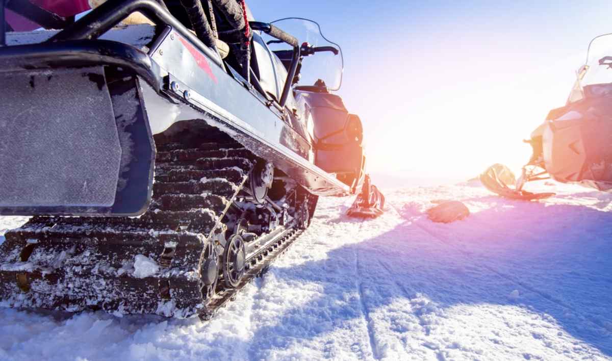 Primo piano dei cingoli di una motoslitta parcheggiata su neve brillante al sole.
