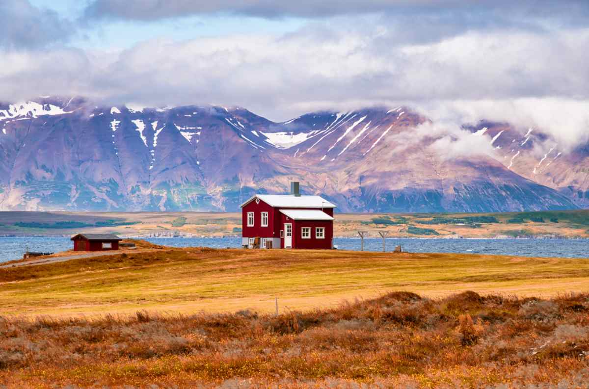 Casa rossa nordica Casetta rossa isolata su fiordo islandese con montagne innevate sullo sfondo.