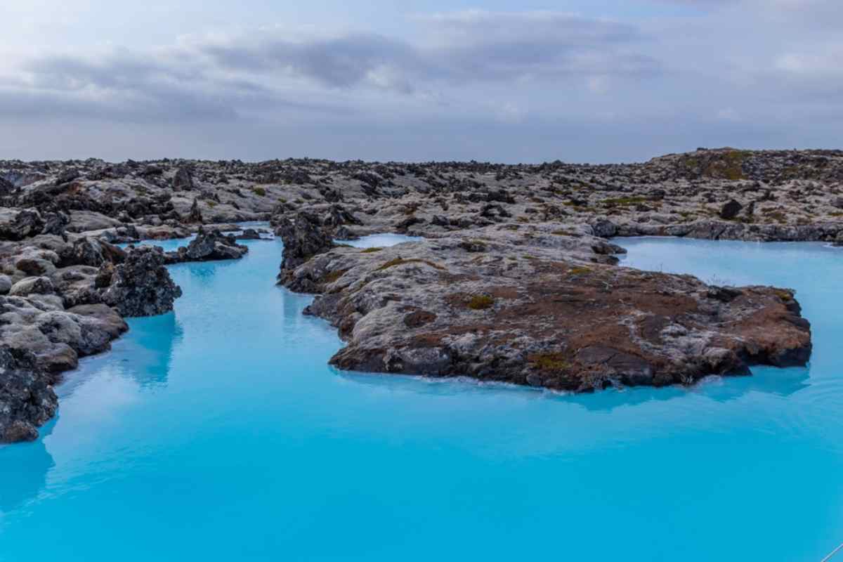Laguna azzurra Vasche geotermiche color turchese tra rocce laviche sotto cielo nuvoloso.