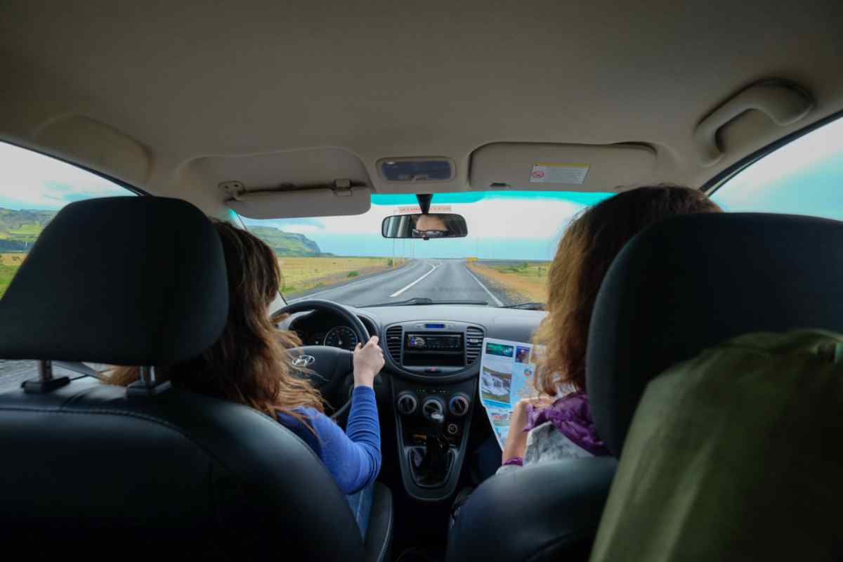 Guida in Islanda Due viaggiatrici in auto sulla Ring Road, vista dal sedile posteriore con mappa in mano.