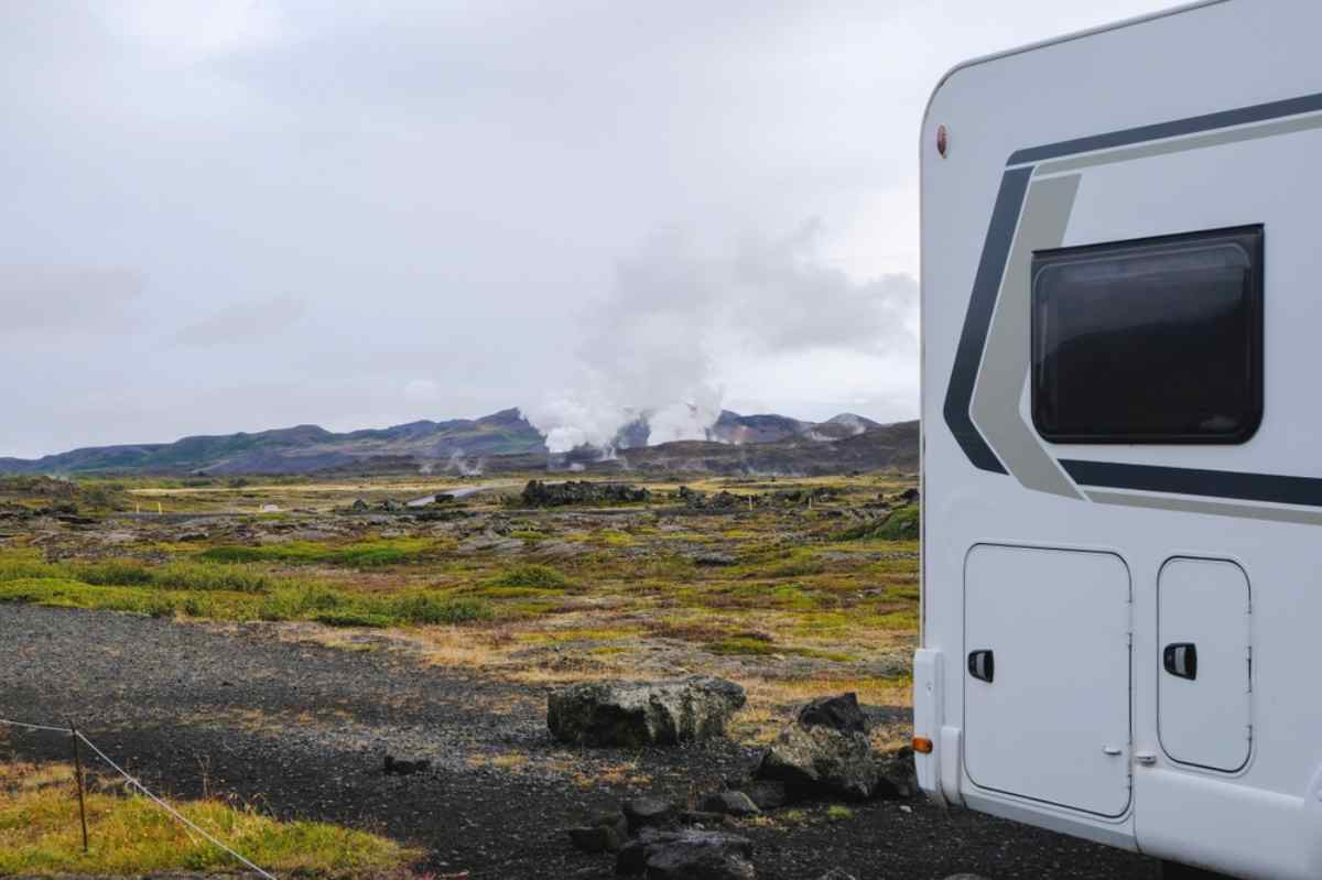 Camper parcheggiato in paesaggio vulcanico d’Islanda con fumarole geotermiche e colline sullo sfondo.