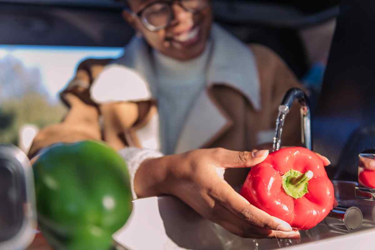 Viaggiatrice che lava un peperone rosso sotto il rubinetto nella cucina del camper.